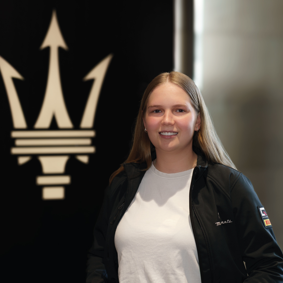 Junge Frau lächelt vor einem Maserati Logo im Hintergrund