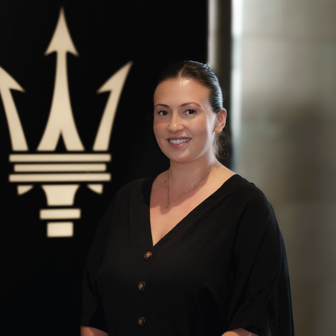 Frau in schwarzem Outfit vor einem Luxusautologo lächelnd