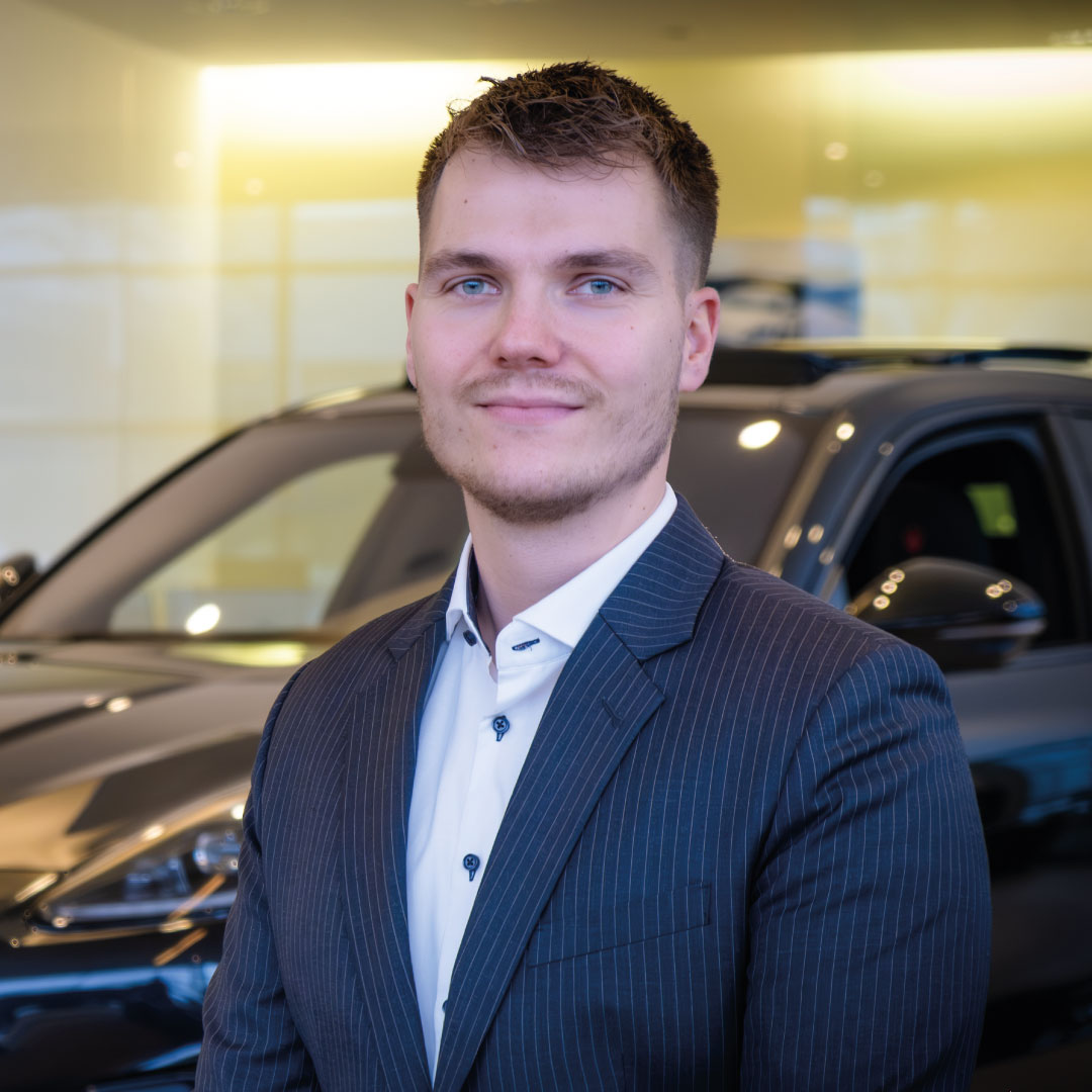 Geschäftsmann in Anzug steht vor einem schwarzen Auto im Büro