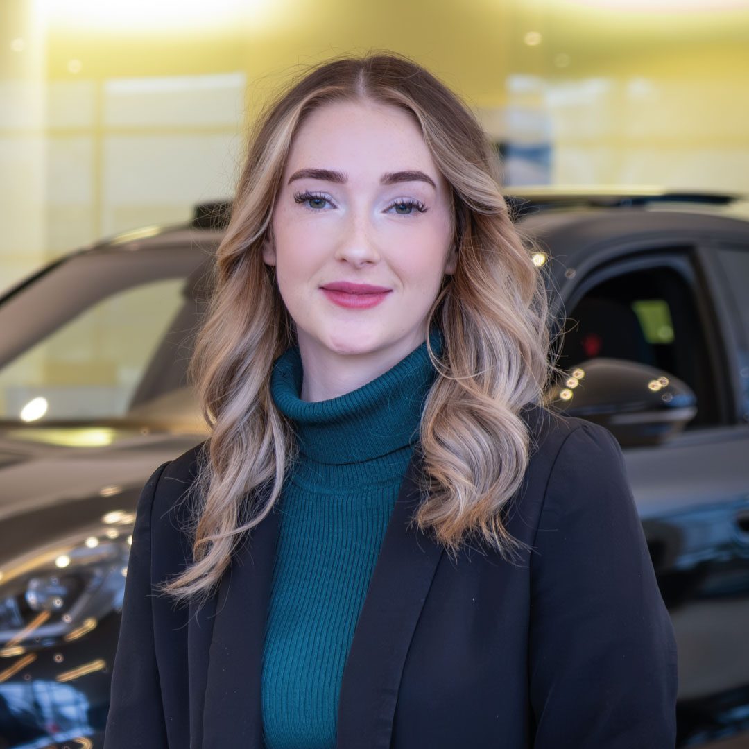 Junge Frau lächelt vor einem modernen Auto im Ausstellungsraum