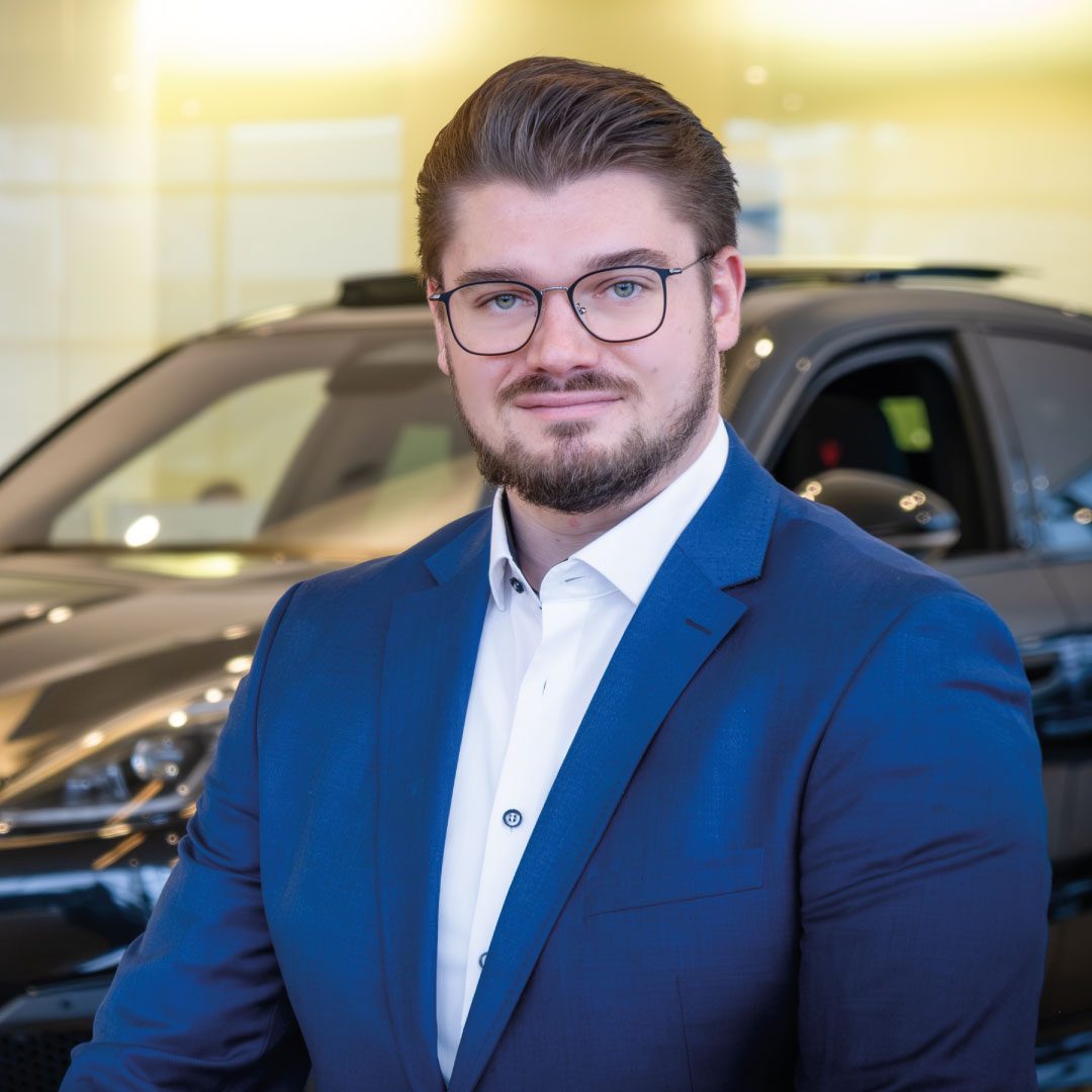 Mann im blauen Anzug vor schwarzem Auto im Showroom