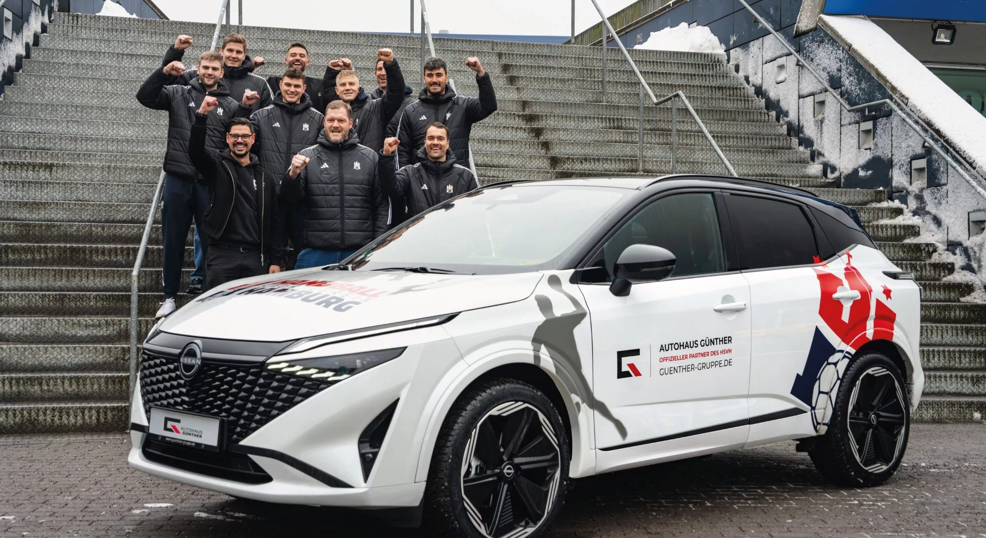 Gruppe jubelt neben neuem weißem Auto auf Treppe stehend