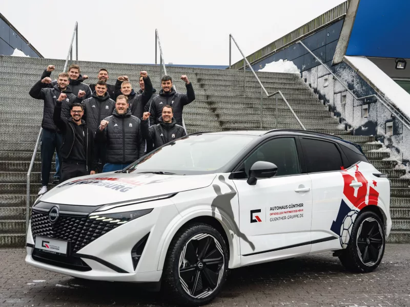 Team posiert mit gebrandetem Auto vor großer Treppe im Freien